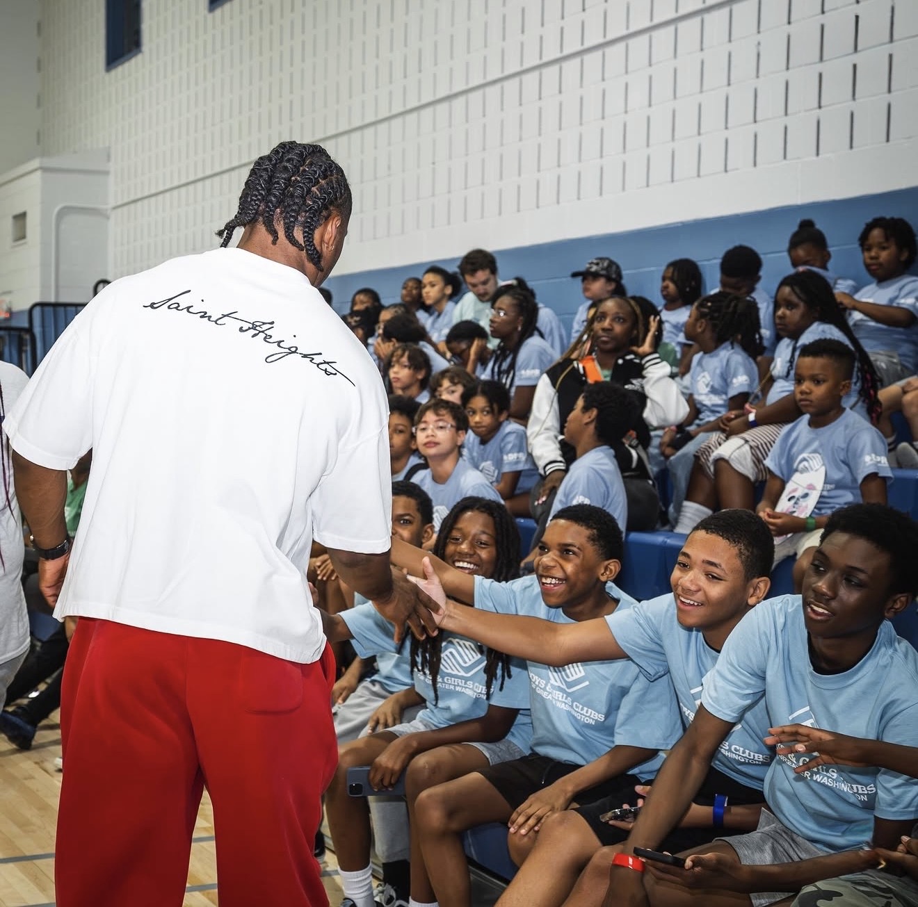 Nick Cross high-fiving a full set of bleachers of Boys & Girls Clubs kids