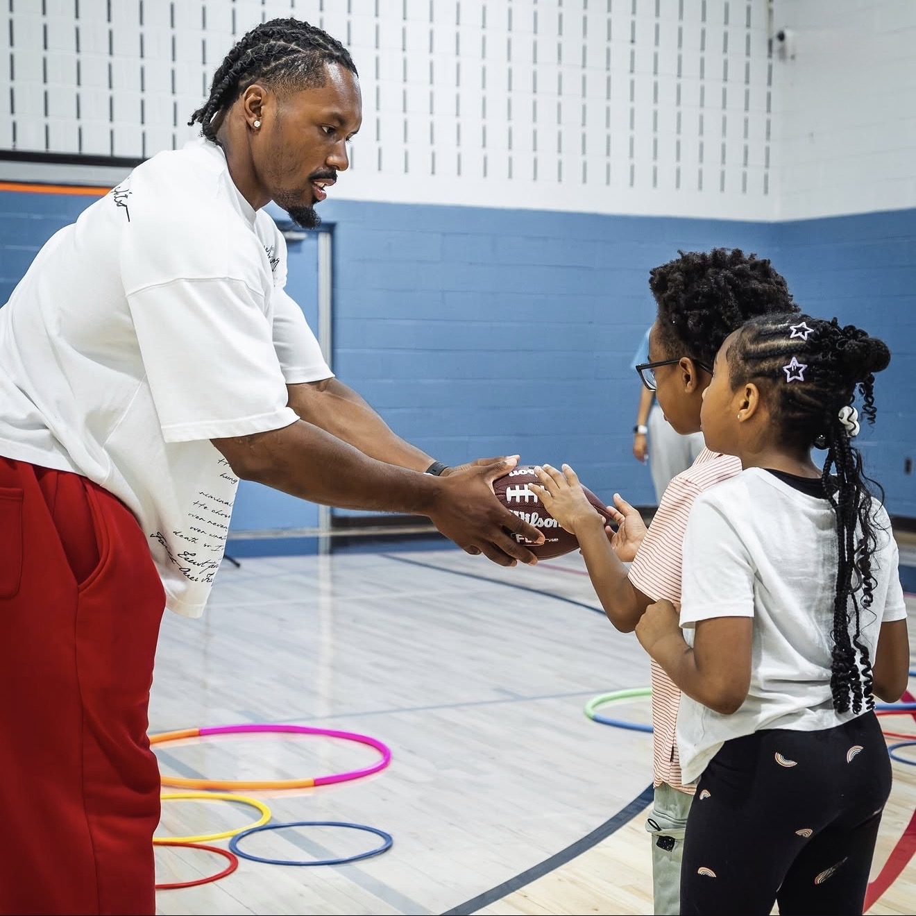 Nick Cross handing a football to two young kids at the Boys & Girls Clubs gym