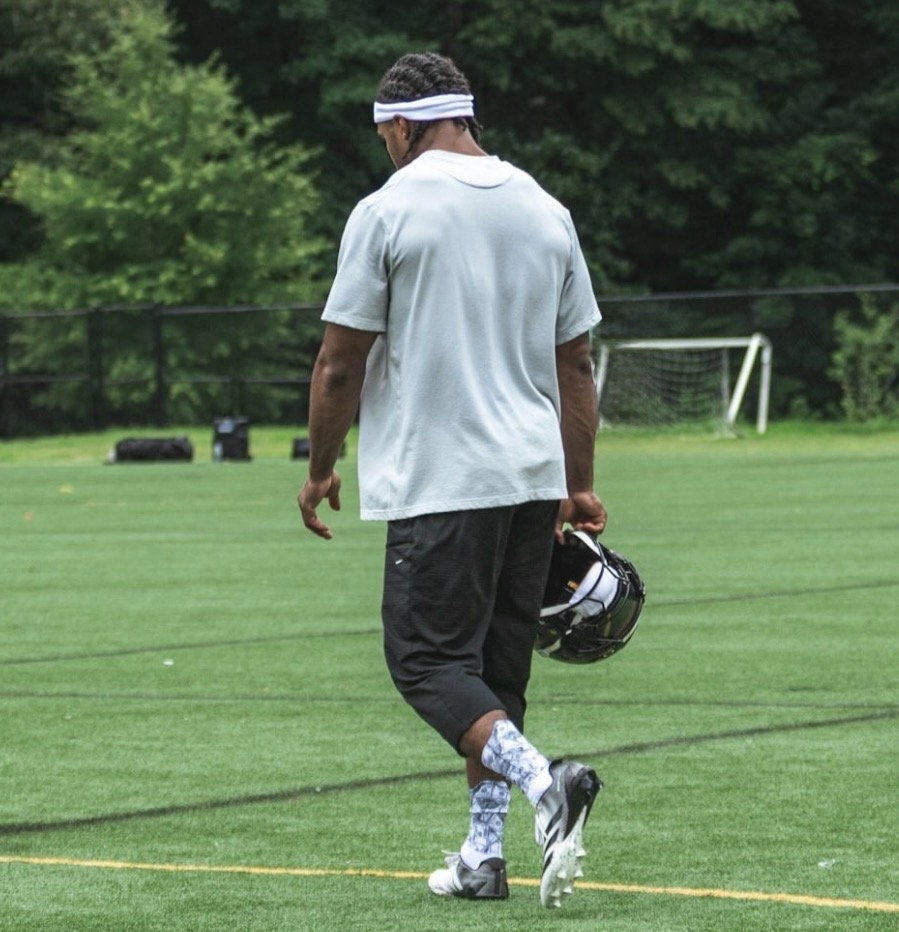 Nick Cross walking across a practice field carrying his helmet, seen from behind