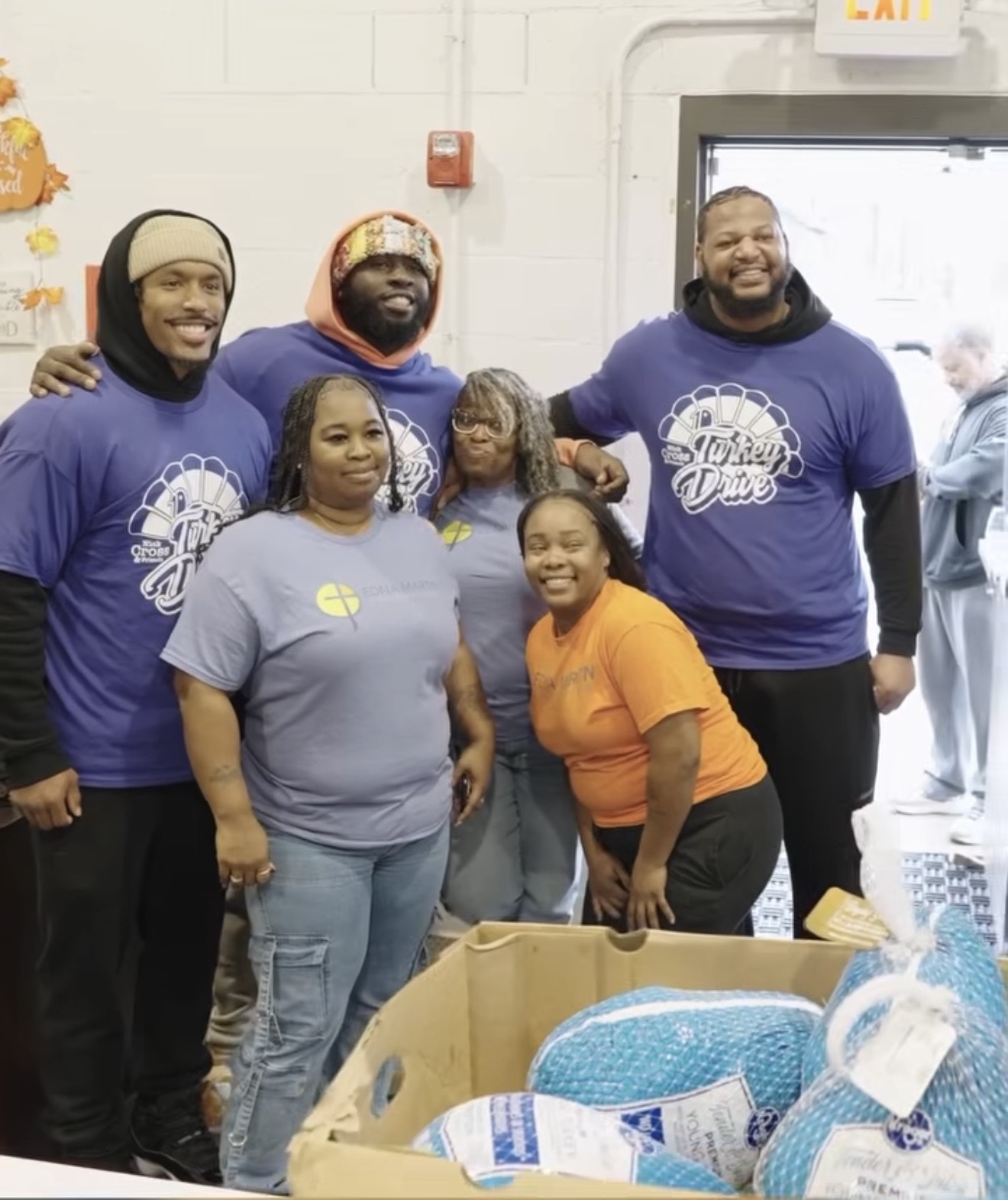 Nick Cross and volunteers in Turkey Drive shirts smiling behind a box of frozen turkeys